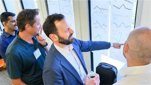Three professionals collaborating and smiling while looking at a laptop during an interactive session.