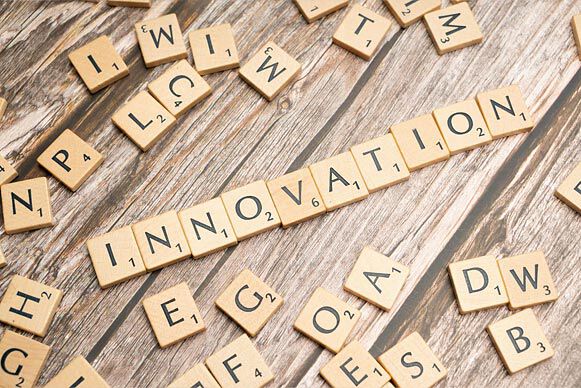The word ‘Innovation’ spelled out with wooden Scrabble tiles on a rustic wooden surface.