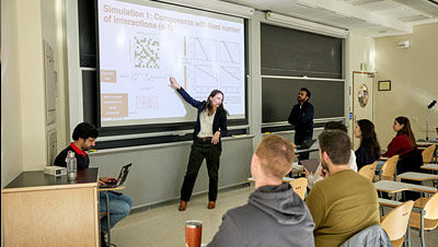 nstructor presenting a scientific simulation on a projector screen to a classroom of seated students.