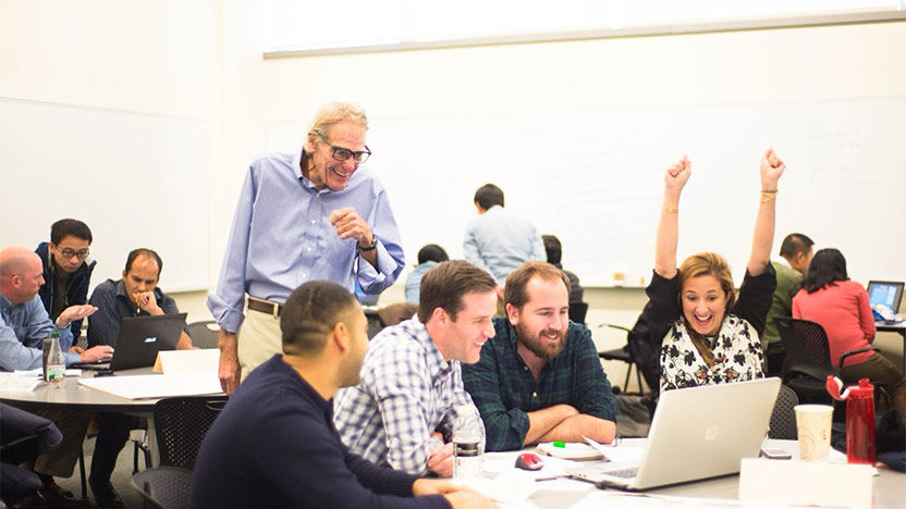 Excited executive education participant raising hands in celebration with team and faculty member observing.