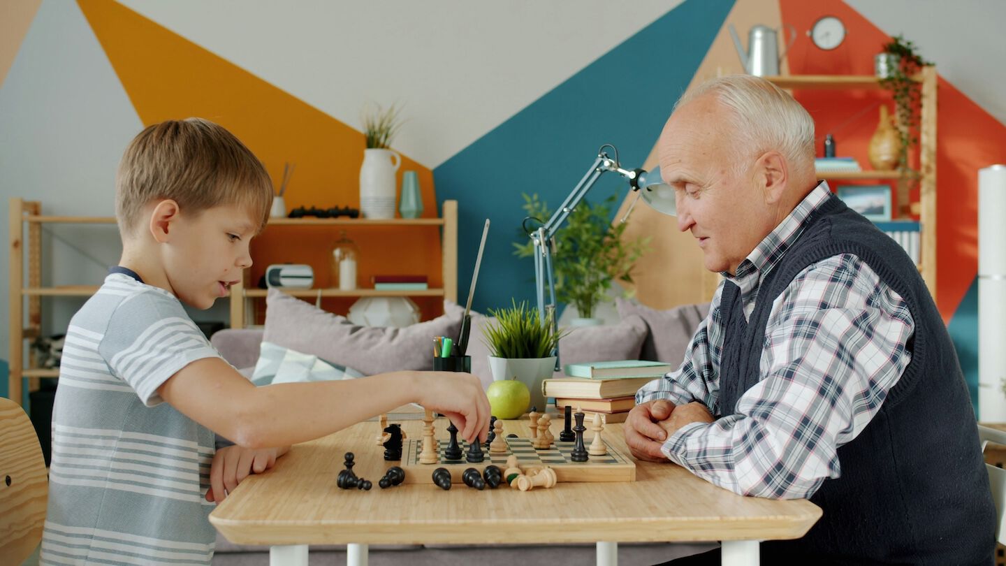 photo of a child and older man playing chess at a table