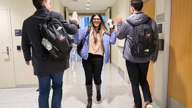 Three students in winter clothing high-fiving in a hallway at MIT Sloan.