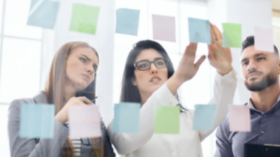 three persons behind a glass wall looking at post it notes on it