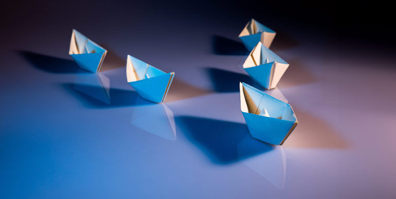 Group of five folded paper boats on a reflective blue surface, symbolizing leadership and direction.