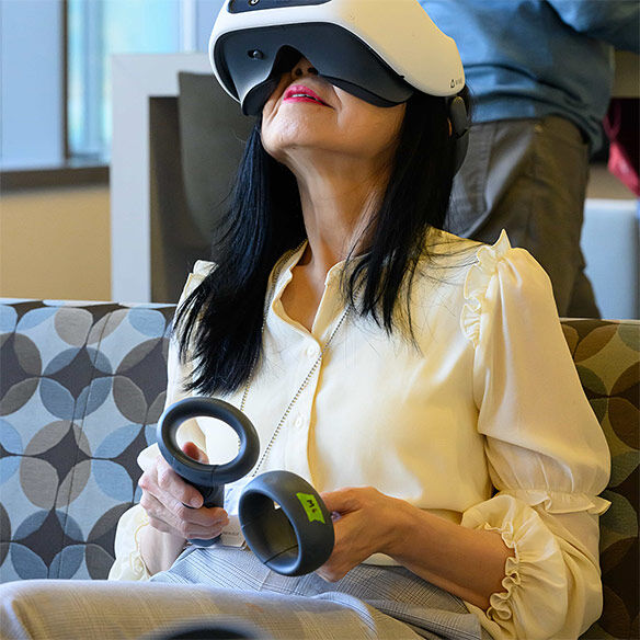 Woman wearing a virtual reality headset and holding controllers while seated in a tech-enabled space.