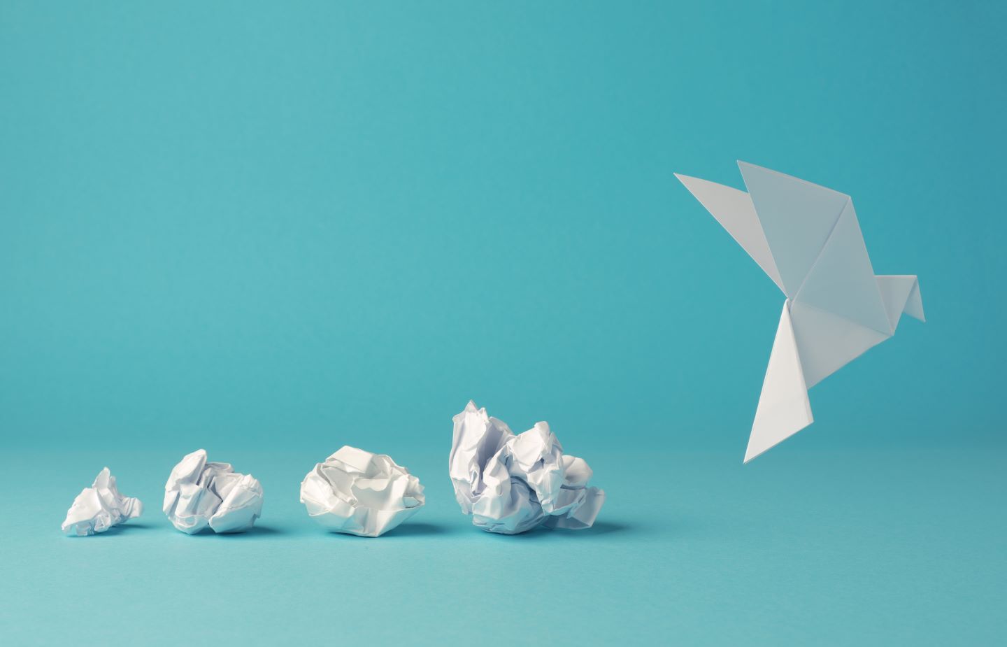 four balls of scrunched up paper getting progressively bigger, and a fifth one on the right that is a bird origami flying away