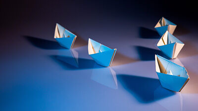 Group of five folded paper boats on a reflective blue surface, symbolizing leadership and direction.