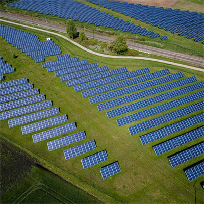 Aerial view of a large solar farm with rows of blue solar panels on green fields.