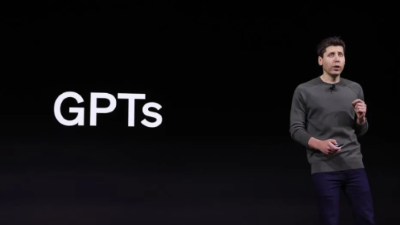 photo of a man on stage with "GPTs" spelled next to him