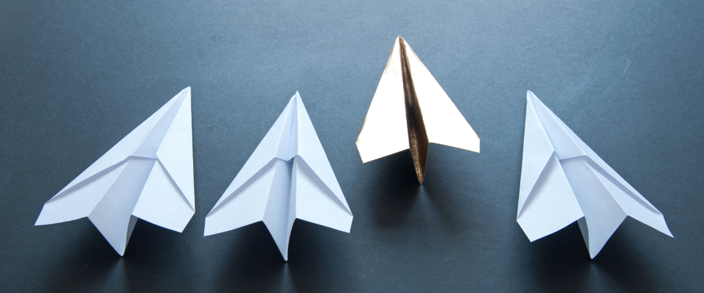 one gold paper airplane ahead of three white paper airplanes