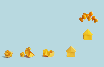 Paper house floating from being tied to balloons with other house behind.