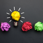 Crumpled paper balls of different colors with one representing a lightbulb.