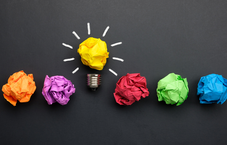 Crumpled paper balls of different colors with one representing a lightbulb.