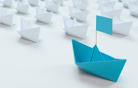 White paper boats in a row with single blue boat in front.