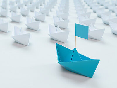 White paper boats in a row with single blue boat in front. image number null