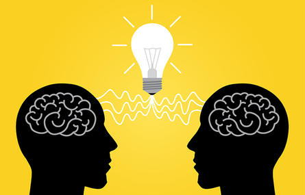 Silhouette of two heads facing each other with light bulb lit up in between them.