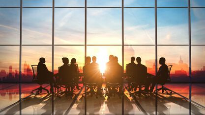 photo of a group of people sitting around a table behind a glass wall in a building and the sunset behind them image number null