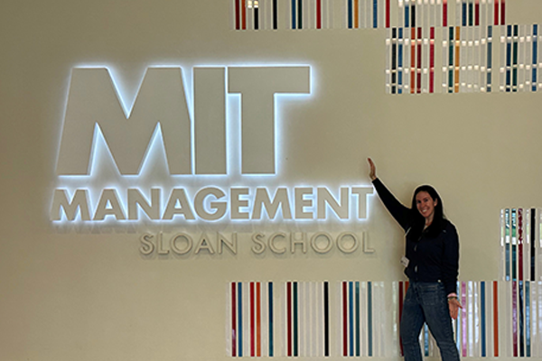 Jillian stands in front of the MIT Sloan School of Management wall sign inside building E62