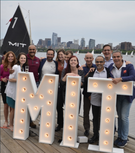  Program alumni holding light up MIT sign on a deck overlooking Boston.